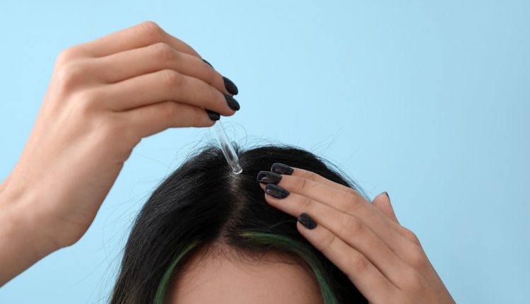 Young woman using serum for hair loss treatment on color backgro