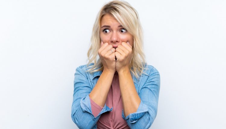 Young blonde woman over isolated white background nervous and scared putting hands to mouth