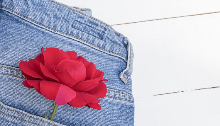 Flat lay with blue jeans and red rose flower on white wooden table