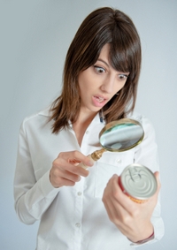 Shocked young woman inspecting a can’s nutrition label with a magnifying glass