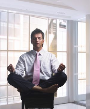 Businessman relaxes in office in traditional lotus pose. Daylight, indoor, office.