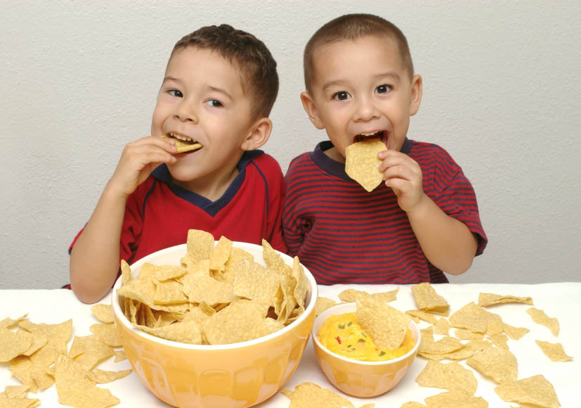 Two preschool brothers have fun enjoying a huge bowl of tortilla chips and some queso.