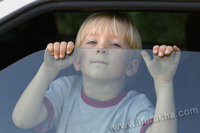 Boy  looking out of a car, dirty hands gripping the top edge of window