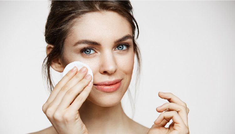 Cute beautiful natural brunette girl cleaning face with cotton sponge smiling looking at camera over white background. Cosmetology and spa.